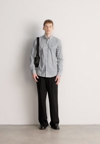 Πουκάμισο με ρίγες σε ανοιχτό μπλε και λευκό, μαύρο παντελόνι και μαύρα παπούτσια. Μια μικρή μαύρη τσάντα χιαστί κρέμεται από τον ώμο.