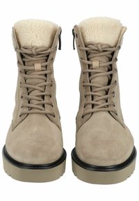 Botas de ante color canela con un forro de felpa beige, ojales negros y suelas de goma beige. Presentan cordones en la parte frontal y un diseño de puntera redondeada.