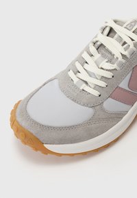 Szare zamszowe i siateczkowe sneakersy z gumową podeszwą, z kremowymi sznurówkami i jasnoszarymi akcentami, w tym różowym elementem wzorniczym.