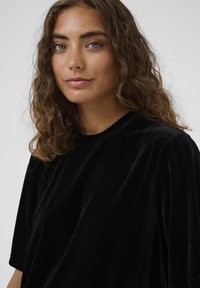 Melna noseguma krekls ar īsām piedurknēm, apaļu izgriezumu un maigu, gludu tekstūru. Audums nedaudz atstarot gaismu.