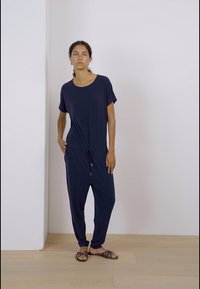 Námořnický overálek s krátkými rukávy, stahovací pas a zúžené nohavice, vyrobený z měkké tkaniny. Model nosí vzorované sandály.