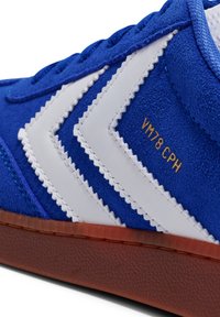 Baskets en daim bleu avec des bandes blanches en zigzag, semelle en caoutchouc marron, et texte doré "VM78 CPH" sur le côté. Finition texturée et détails cousus.