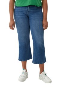 Denim culottes u srednje plavoj boji, s raširenim oblikom, klasičnim dizajnom s pet džepova i sirovim rubom, uparenim s bijelim tenisicama.