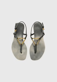Sandali neri flat con accenti dorati, design a T, parte superiore in pelle, suola grigia opaca, stile minimalista, caratterizzati da cinturini sottili e dettagli di cucitura.