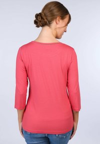 Korallfarbener Langarmshirt mit rundem Ausschnitt und einem strukturierten Stich am Rücken. Das weiche Material fällt sanft über den Körper.