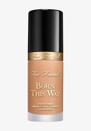 Too Faced Born This Way Foundation in einer beigen Flasche. Verfügt über einen schwarzen Deckel, goldene Akzente und den Text „Foundation mit mittlerer bis voller Deckkraft“.