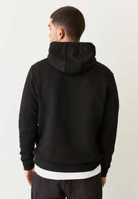 Felpa con cappuccio nera con tessuto strutturato, cappuccio foderato e polsini a costine. Il design presenta una silhouette aderente e un orlo dritto.