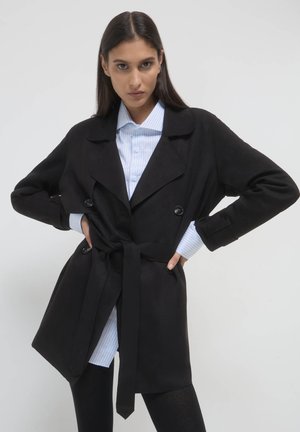 Manteau noir en trench avec une taille ceinturée, grands revers et deux boutons, superposé sur une chemise à rayures bleu clair. Texture de tissu lisse.