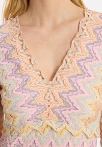 Haut en dentelle avec un décolleté en V, motif en zigzag dans des couleurs pastel comme le pêche, la lavande et la menthe, avec une finition texturée et des bords volantés.