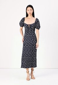 Vestido floral azul marinho com mangas bufantes, decote quadrado e detalhe em gota na parte da frente. Silhueta longa e justa com um acabamento fluido.