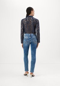 Haut en dentelle marine à manches longues avec un motif floral, associé à un jean skinny bleu clair. Comprend une ceinture élégante et des sandales à talons.