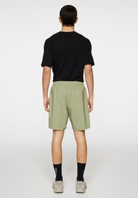 Mustat, tekstuurilla varustetut lyhythihaiset paidat on yhdistetty vaaleanvihreisiin shortseihin, joissa on joustava vyötärö. Asusteena mustat sukat ja beiget lenkkarit.