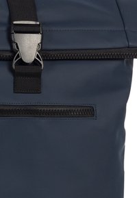 Marineblauwe rugzak met een gestructureerd, waterafstotend oppervlak, een bovenste sluiting en een ritszak aan de voorkant met zwarte hardware.