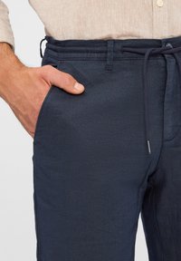 Marineblaue Leinenhosen mit einem Kordelzugbund, das eine glatte Textur und eine Seitentasche aufweist. Der Stoff wirkt leicht und atmungsaktiv.