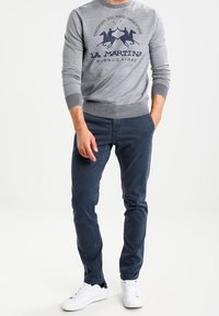 Maglione grigio con colletto tondo, caratterizzato da una grafica testuale blu navy. Abbinato a pantaloni slim-fit blu scuro e sneakers bianche.