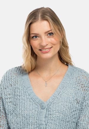 Silberne Halskette mit ineinander verwobenen Schlaufen, getragen über einer hellblauen, gestrickten Strickjacke mit Knopfdetails und weitem Ausschnitt.