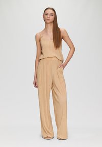 Beige Plissee-Top und weit geschnittene Hose aus leichtem Stoff. Mit dünnen Trägern und lockerer Passform, außerdem mit Taschen an der Hose.