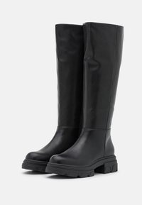 Black knee-high boots made of smooth leather, featuring a chunky rubber sole with a patterned tread and a slightly slouchy design.