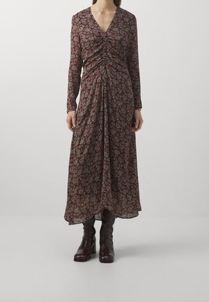 Femme portant une robe midi à manches longues, col en V, froncée, avec un motif floral sombre, associée à des bottes à talons marron foncé.