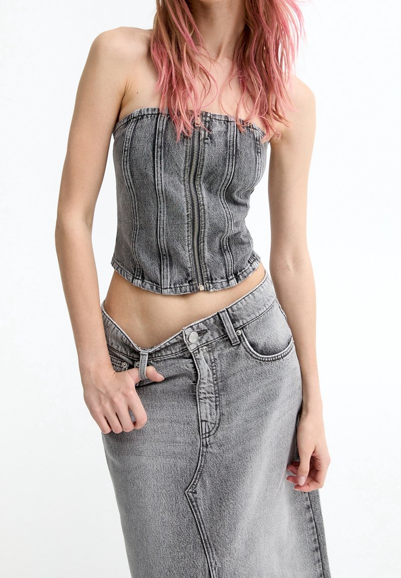 Grijze denim strapless top met verticale naden, voorzien van een voorkeursrits. Gecombineerd met een bijpassende grijze denim rok, die een gecoördineerde look benadrukt.
