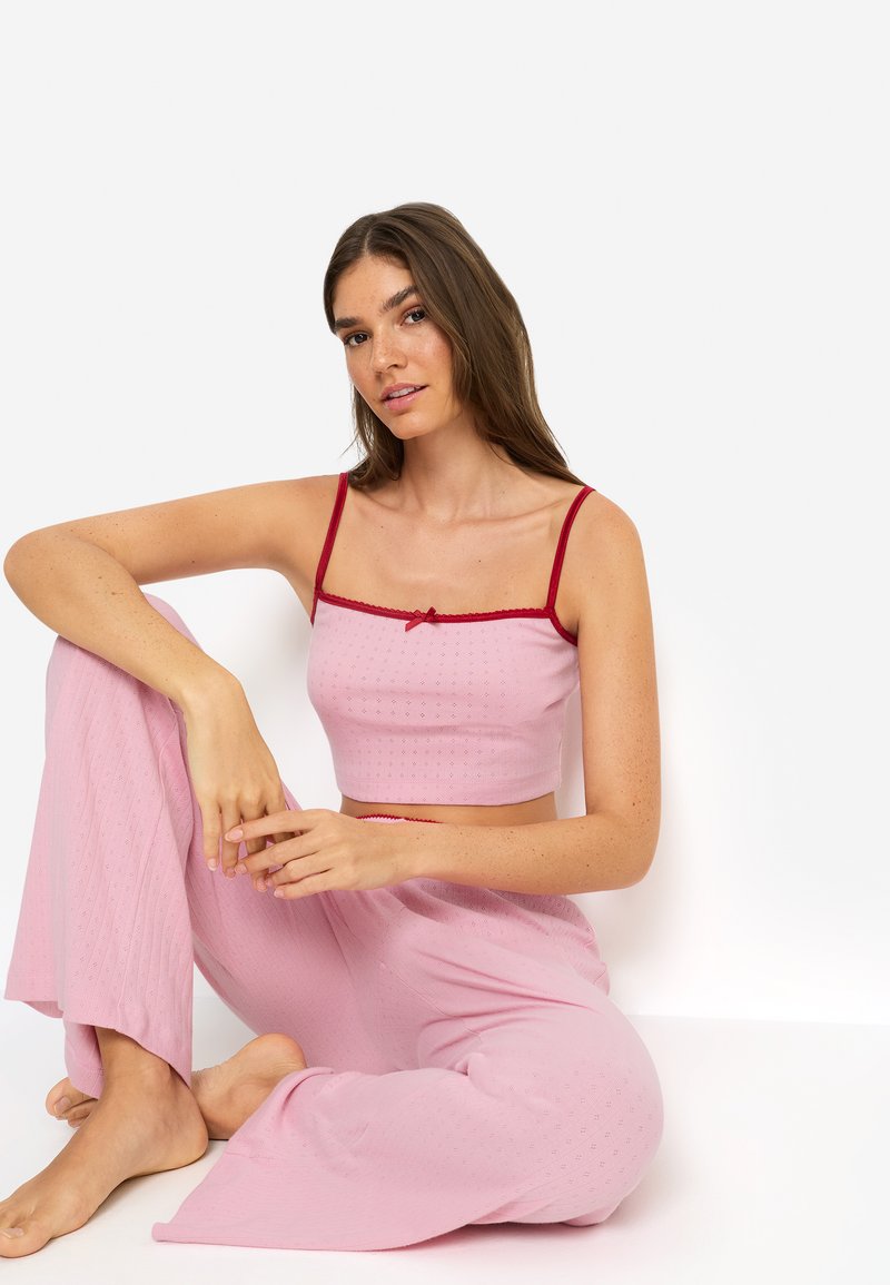 Ροζ κροπ τοπ με κόκκινο περίγραμμα και φιόγκο, σε συνδυασμό με παντελόνι με φαρδιά πόδια και ανάγλυφο μοτίβο. Λείο ύφασμα, casual σχεδιασμός.