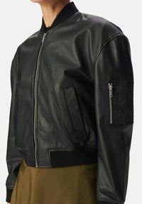 Zwarte leren bomberjack met ribgebreide kraag, rits aan de voorkant, zijzakken en een ritszak op de arm. Gladde textuur, cropped design.