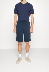 T-shirt à manches courtes bleu marine associé à un short bleu marine. Le short présente une taille élastique et un cordon de serrage. Des baskets beiges complètent la tenue.
