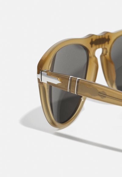 Bruna genomskinliga solglasögon med grå linser, med en unik form, eleganta metallen detaljer och ett mönstrat skalmdesign.