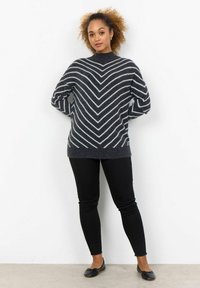 Pull en tricot à motif chevron gris, à col haut, manches longues et texture douce, associé à un pantalon noir slim et des chaussures plates.