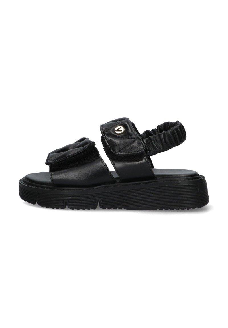 Zwarte leren sandaal met een gestructureerde afwerking, elastische band aan de achterkant en een decoratieve plooi bovenaan. Heeft een dikke rubberen zool.