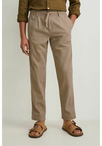 Pantalon marron clair, léger, élastiqué avec un cordon de serrage, poches latérales et coupe décontractée, associé à des sandales marron.