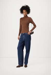 Braun eng anliegender Rollkragenpullover mit Blumenmuster, kombiniert mit hoch taillierten blauen Denim-Jeans. Die Accessoires umfassen eine kleine braune Handtasche.