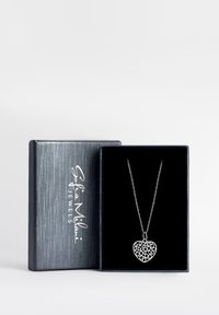 Sølv hjertevedhæng i halskæde med intrikate udskæringer på en fin kæde, præsenteret i en gaveæske med sort fløjl.