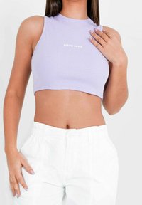 Fialový žebrovaný crop top s vysokým výstřihem a bílým logem "SIXTH JUNE" umístěným ve středu hrudníku; zkombinováno s bílými volnými kalhotami.