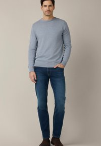 Jasnoniebieski sweter z dzianiny z okrągłym dekoltem, zestawiony z ciemnoniebieskimi dopasowanymi dżinsami. Stylizacja cechuje się gładką fakturą i swobodnym fasonem.