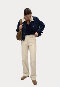 Jeansjacka med krämfärgad krage, marinblå topp, krämfärgade vida byxor och bruna skor. Enkel design, matta texturer och neutrala färger.