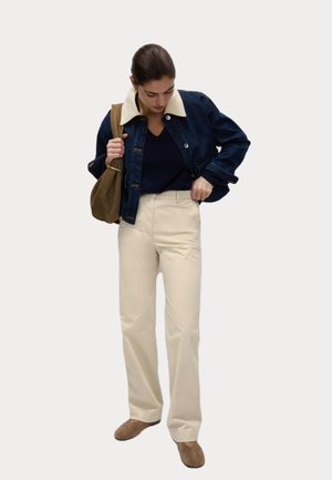 Denimjack met een crèmekleurige kraag, marineblauw bovenstuk, crèmekleurige broek met wijde pijpen en bruin schoeisel. Eenvoudig ontwerp, matte texturen en neutrale kleuren.