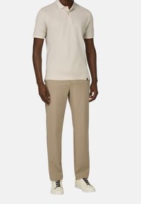 Beige polo skjorta med korta ärmar, knäppt krage; kombinerad med ljusbeige byxor och vita sneakers med svarta snören.