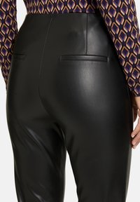 Pantalones de cuero negro con cintura alta, con bolsillos traseros. La tela tiene una textura suave y brillante y un corte entallado.