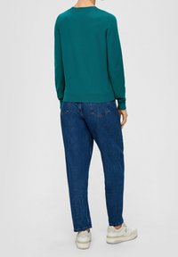 Suéter verde azulado de manga larga y dobladillo acanalado combinado con jeans de corte holgado en azul oscuro y zapatillas blancas. Diseño simple y ajuste clásico.