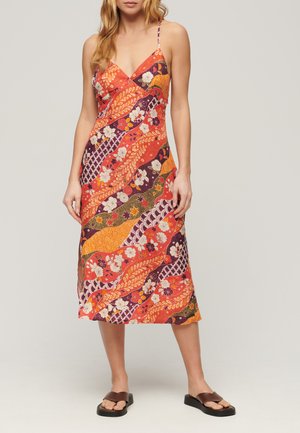 Abito maxi con un vivace motivo floreale e a onde in rosso, arancione e viola. Presenta spalline sottili e un design a V. Includerà sandali piatti.