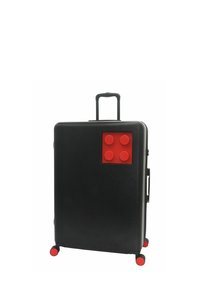 Black suitcase with red LEGO brick design, textured surface, extendable handle, and four red wheels. Notable four raised bricks on front.