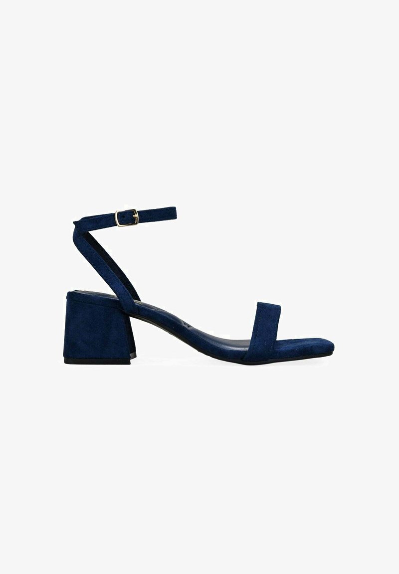 Sandalia de ante azul marino con tacón cuadrado, correa en el tobillo con hebilla dorada y una única correa en el dedo.