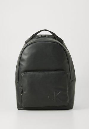 Sac à dos en cuir noir avec poche zippée à l'avant et logo "cK" en relief, poignée supérieure et fermeture à double zip sur fond blanc.