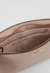 Pochette in pelle rosa chiaro con hardware dorato. L'interno presenta più scomparti e una tasca con zip, stampata con "MICHAEL KORS."