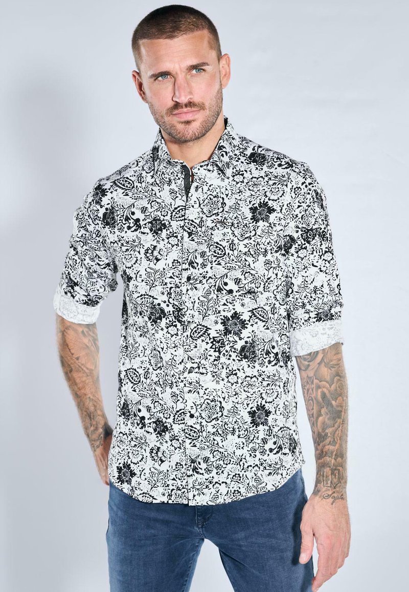Schwarz-weiß gemustertes Hemd mit floralem Design, Knopfleiste und hochgekrempelten Ärmeln, gefertigt aus leichtem Stoff. Verfügt über einen klassischen Kragen.