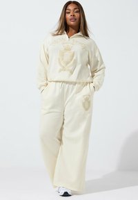 Kremowa, oversize bluza z kapturem z grafiką i emblematem "NEW YORK", zestawiona z dopasowanymi szerokimi spodniami z detalami logo.