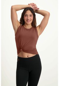 Ruskea hihaton toppi, jossa on solmupisto vyötäröllä, yhdistettynä mustiin korkeavyötäröisiin legginsseihin. Silkkinen kangas, rento muotoilu.