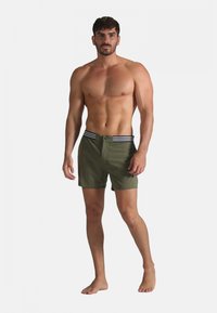 Shorts de bain verts olive avec une ceinture à rayures noires et blanches, dotés d'une fermeture à bouton à l'avant et d'une coupe classique.