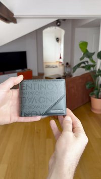 Portofel negru din piele, cu un model texturat diagonal, logo în relief și o formă dreptunghiulară subțire. Design compact pentru transport ușor.